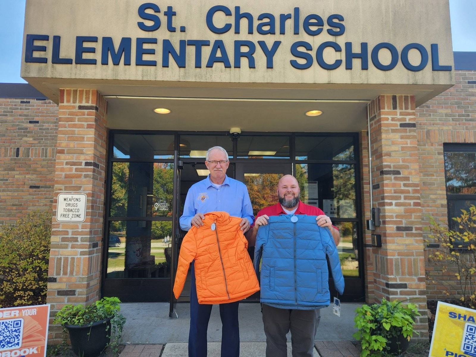 Two men holding donated coats in front of St Charles Elementary School