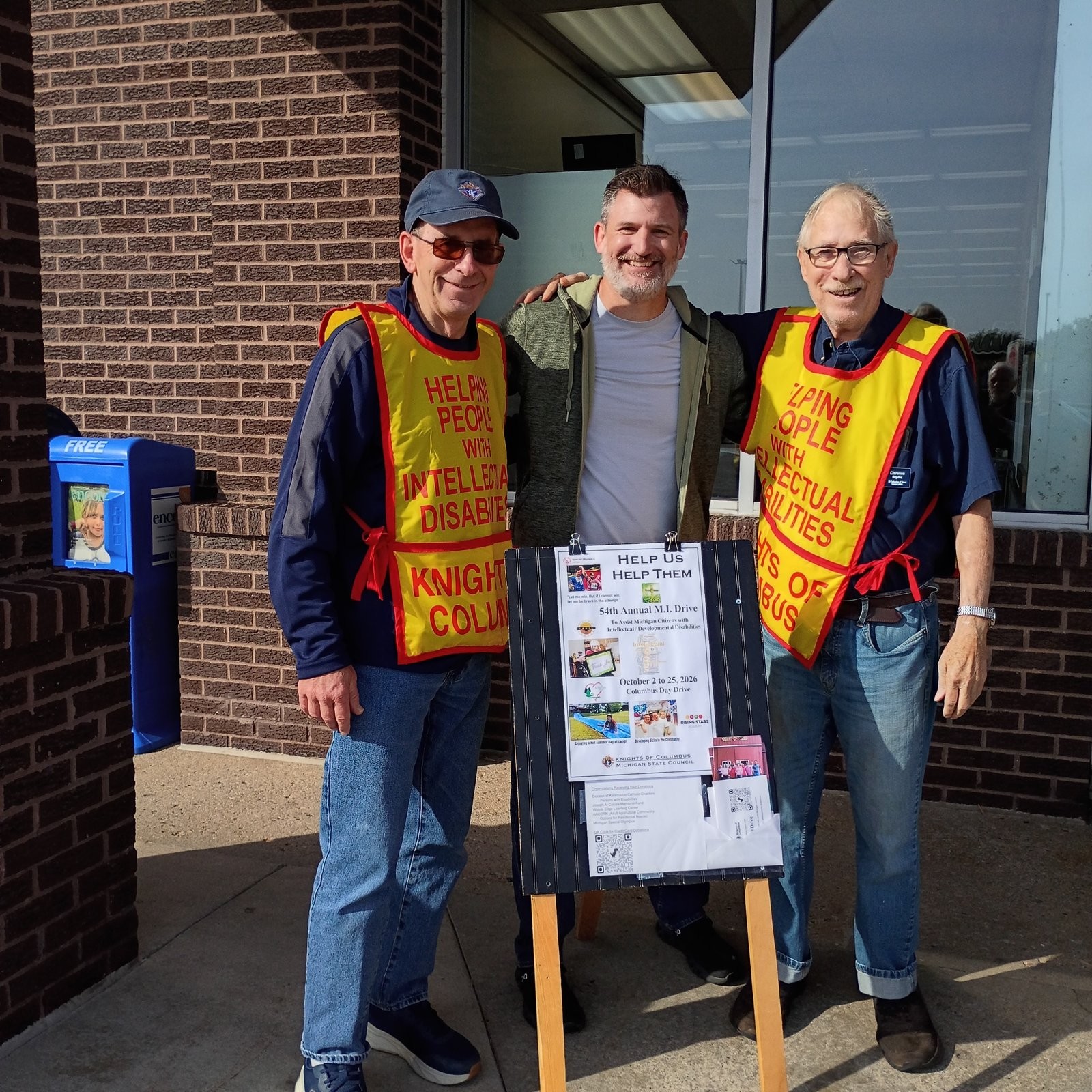 Council 6980 Knights in MI Drive vests beside the Help Us Help Them sign outside a store
