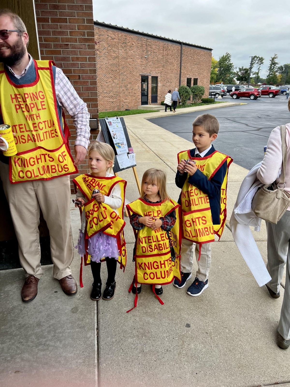 A Knight and young family volunteers in MI Drive vests outside the church after Mass